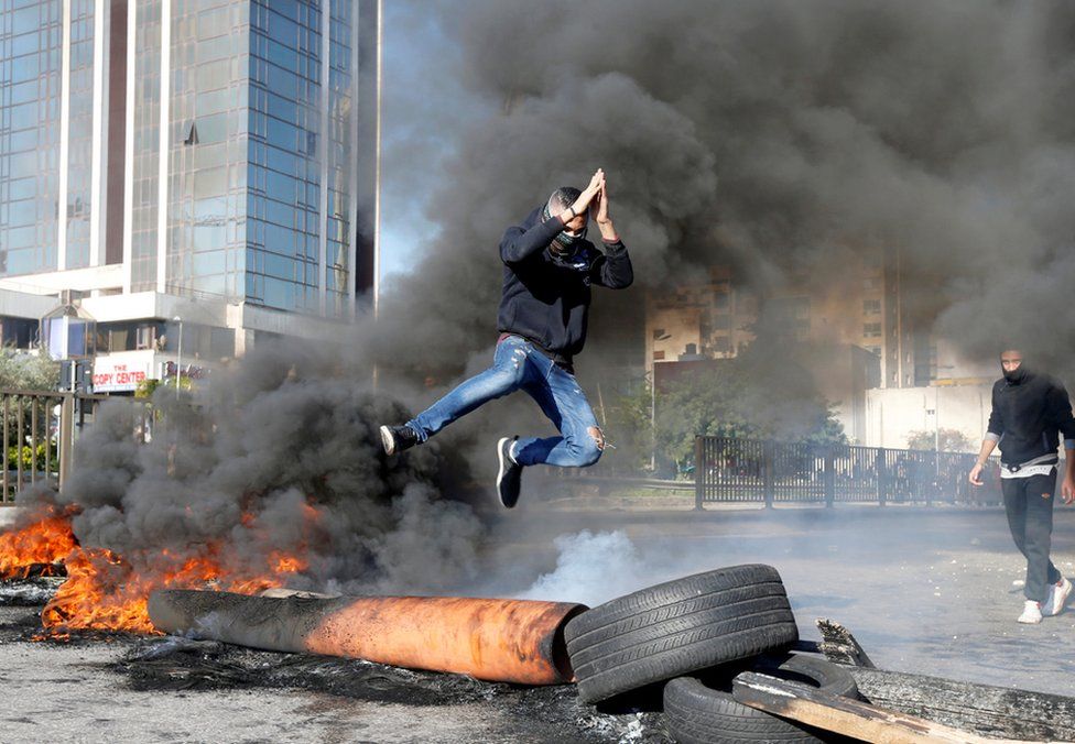 A protestor jumps over a burning barricade during a protest over economic hardship and lack of new government in Beirut