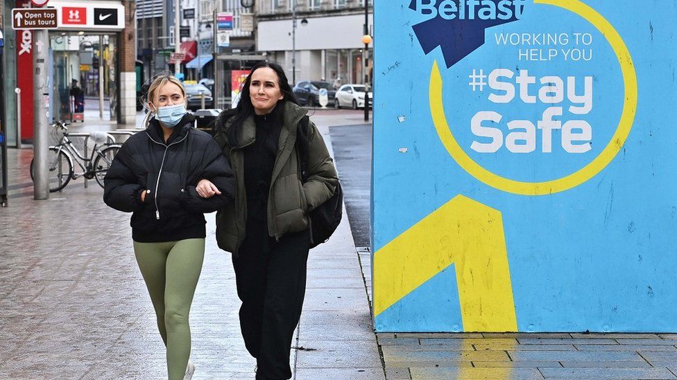 Women walk past a Covid safety sign in Belfast