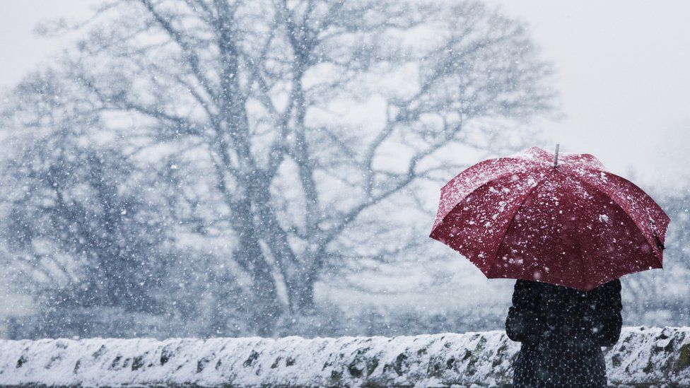 A woman sheltering under a read umbrella in a snow storm