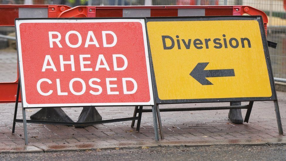 Two A-frame road signs, on left red and white road closed and yellow and black diversion