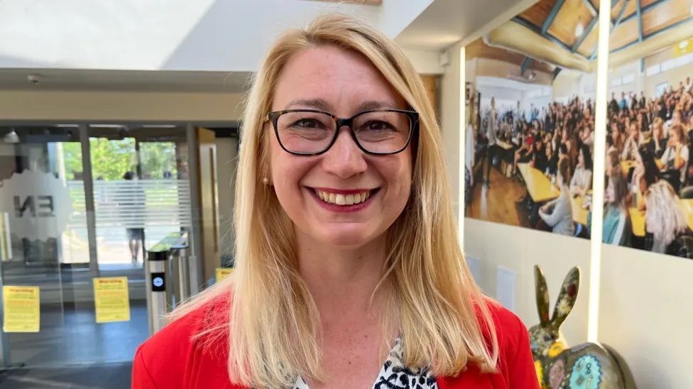 Jess Asato MP wearing a red cardigan and black glasses, smiling