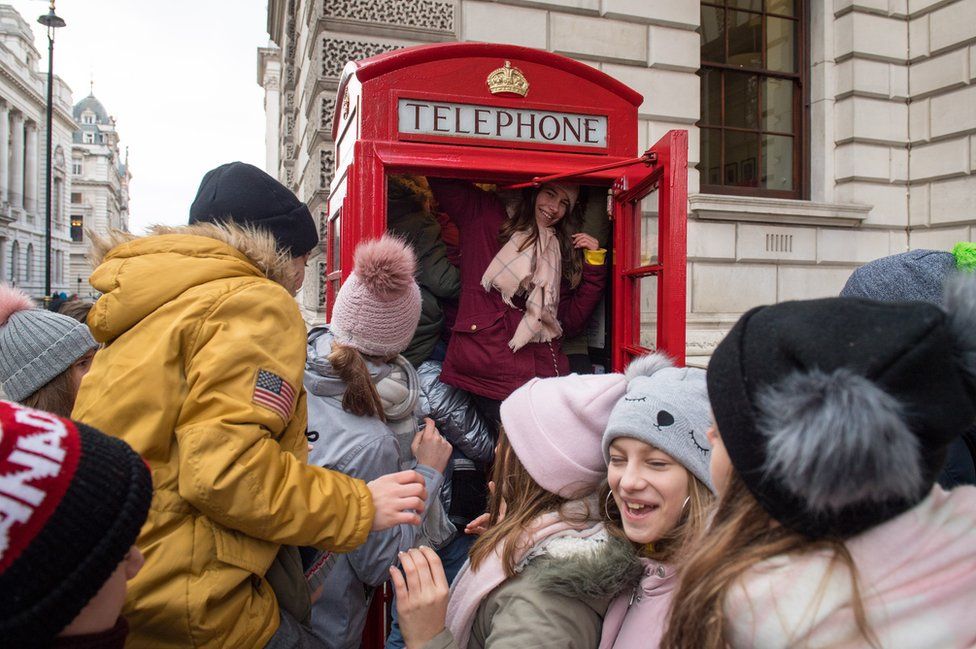 Polish tourists trying to see how many of them can fit into a red telephone box, in Westminster, London