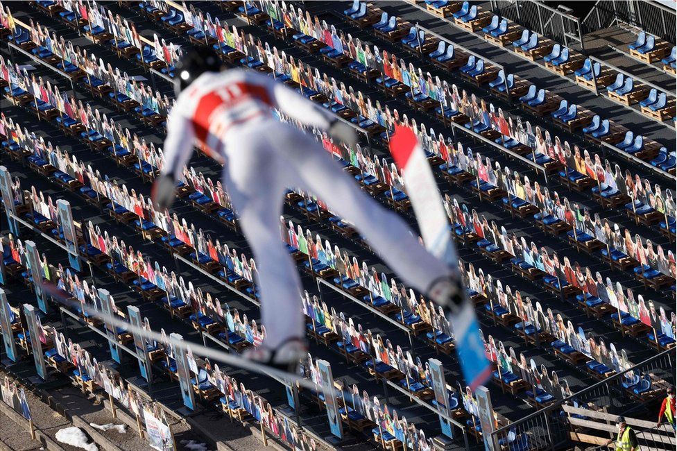 A ski jumper flies through the air with hundreds of cardboard cut outs of people below