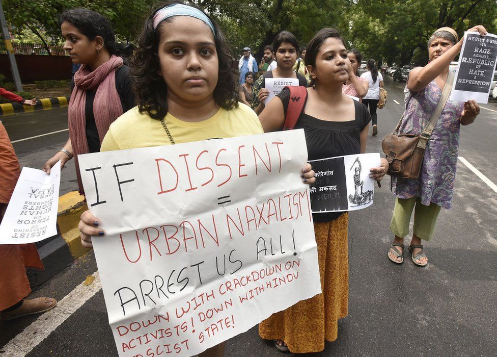 A woman at a protest holding a poster saying, "If dissent = urban naxalism, arrest us all"