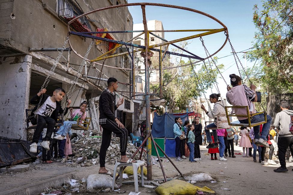 Children sit in a swing as they celebrate on the first day of the Muslim holiday of Eid al-Fitr, after the end of the holy month of Ramadan, in Deir el-Balah in the central Gaza Strip on 10 April 2024