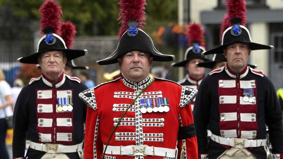 Three members of the Hillsborough Fort Guard - wearing uniform and distinctive feathered hats - stand at attention outside Hillsborough Castle