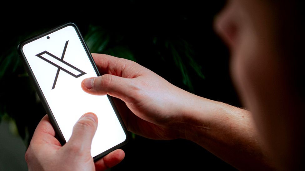 A person holding a phone with the X logo on the screen