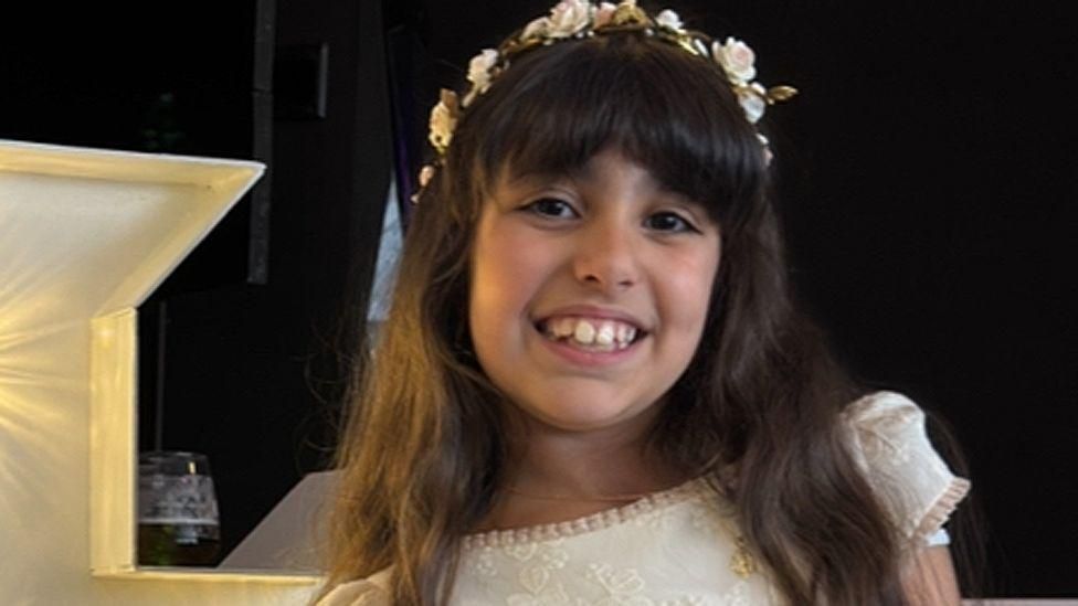 Alice Dasilva Aguiar smiles in a formal dress while wearing a floral garland