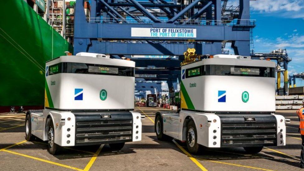 Autonomous white trucks underneath blue metal towers at Felixstowe Port.