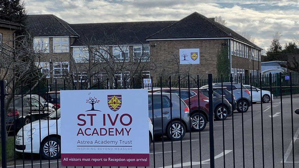 Large brick-built school building with railings in front and "St Ivo Academy" sign