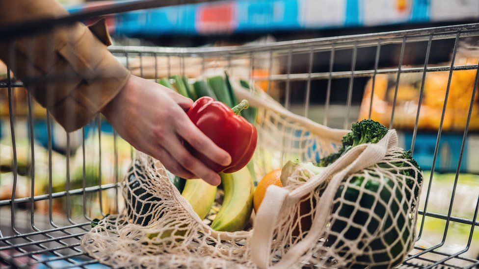 A woman puts a red pepper into a bag in a shopping trolley