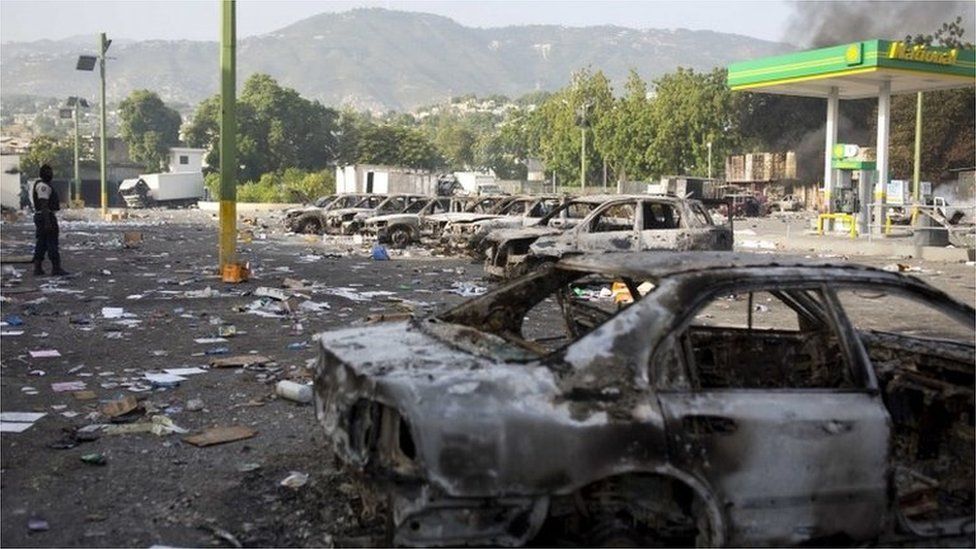 Burned cars sit parked outside the Delimart supermarket complex, near a gas station, after two days of protests against a planned hike in fuel prices in Port-au-Prince, Haiti, Sunday, July 8, 2018.