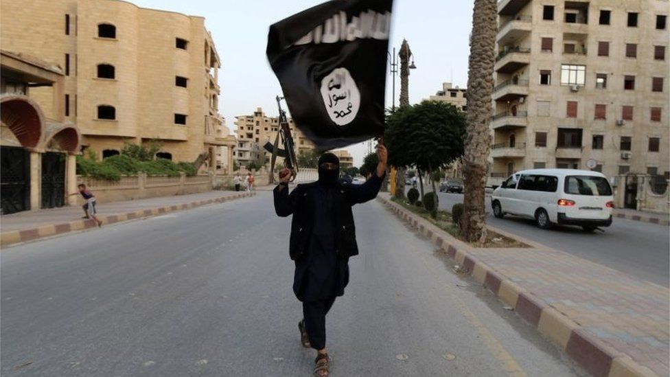 A lone armed and masked Islamic State militant waving an ISIS / ISIL flag, on a deserted street in Raqqa, June 2014