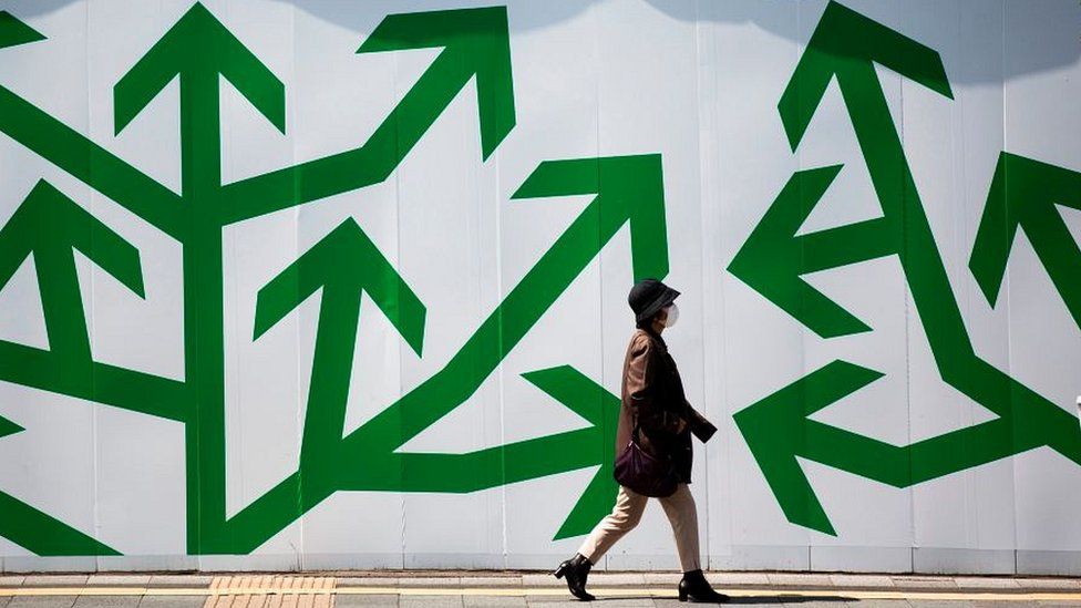A pedestrian walks past decorated panelling used to shroud a construction site along a street in Tokyo