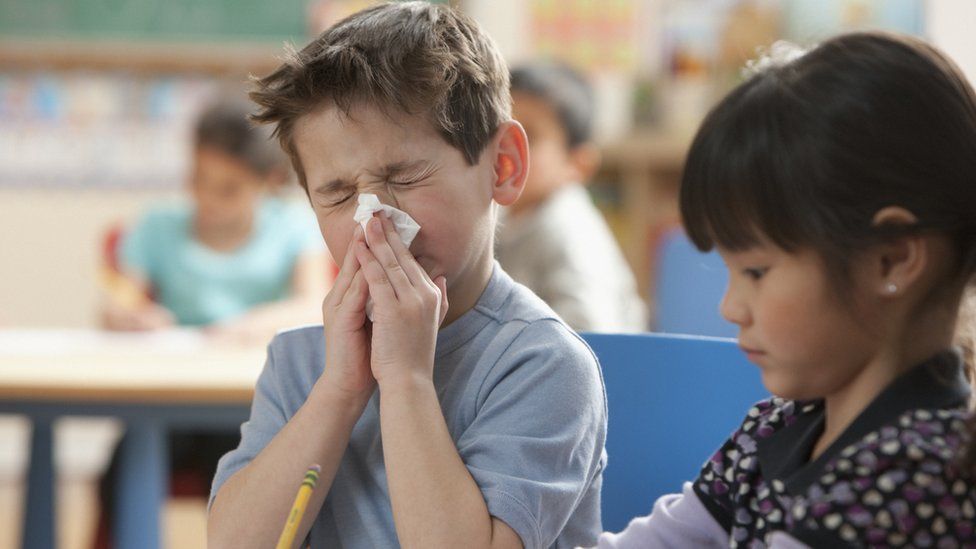 Boy blowing his nose in a classroom