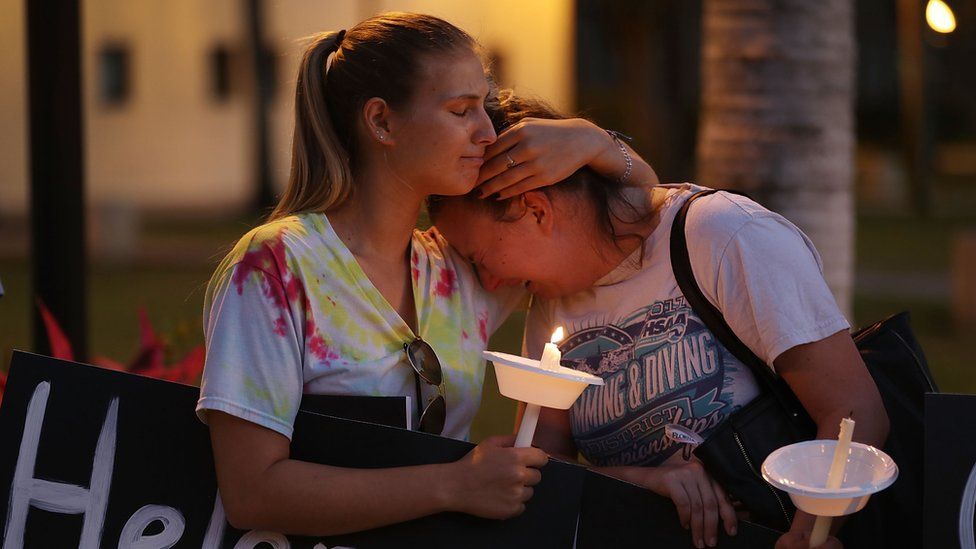 Two women cry at a candlelit vigil