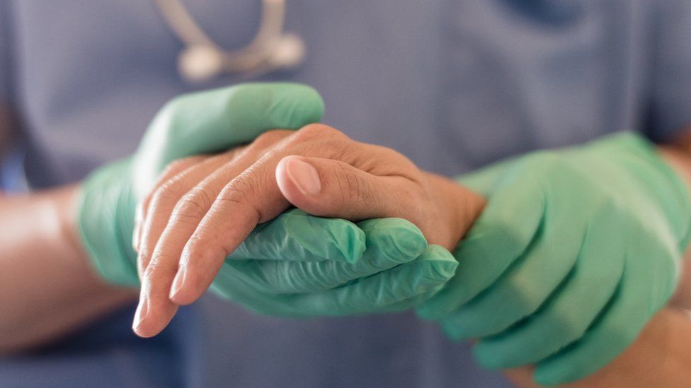 Medical professional wearing gloves holding a patient's hand