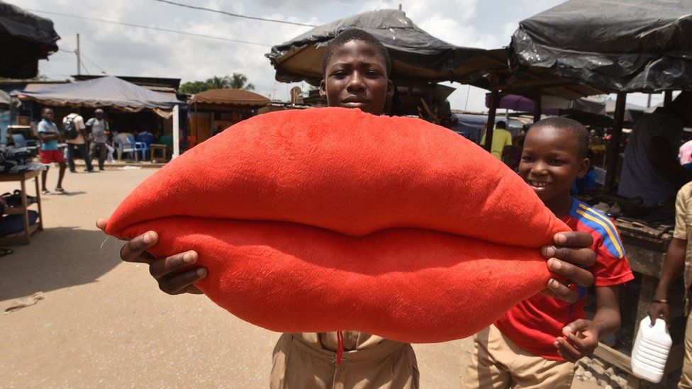 A boy poses with a pillow shaped like lips on sale for Valentine's Day in Yopougon, a suburb of Abidjan, in Ivory Coast - 13 February 2018