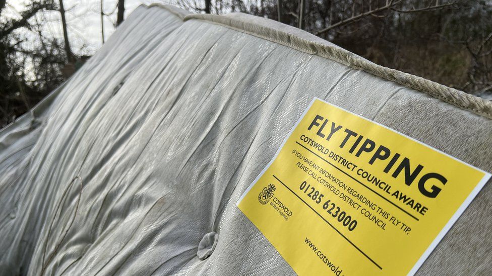 A flytipped mattress with a yellow sticker on it from Cotswold District Council asking for information
