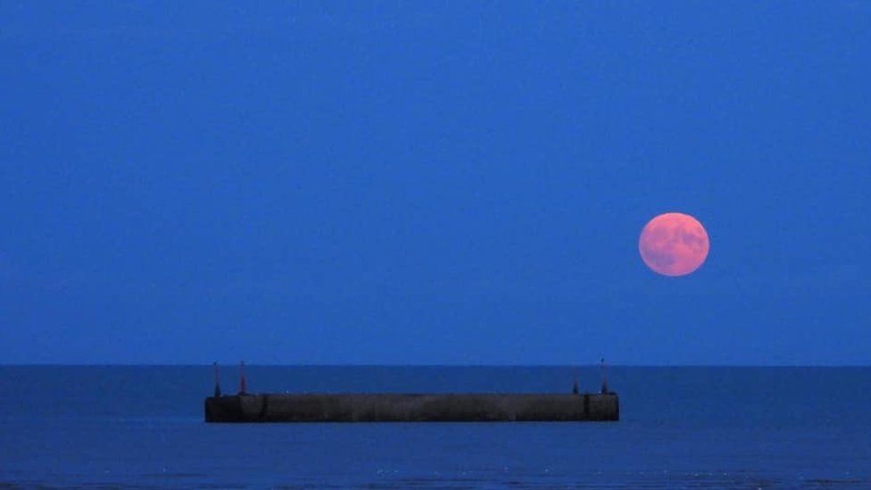 The blue supermoon is red as it rises over Mulberry Harbour in Littlestone-on-Sea, Kent