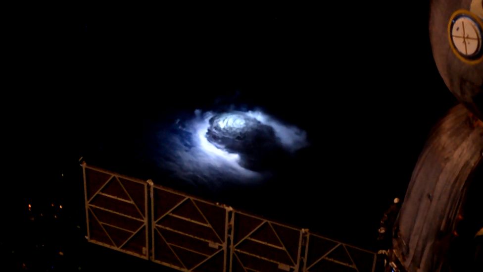 A cloud illuminated by lightning, with a panel of the International Space Station visible at the bottom of the frame