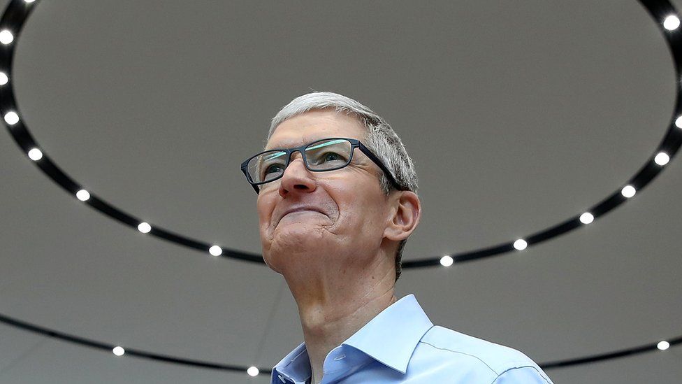 Тим Кук стоит в штаб-квартире Apple, его голова окружена ореолом прожекторов на потолке