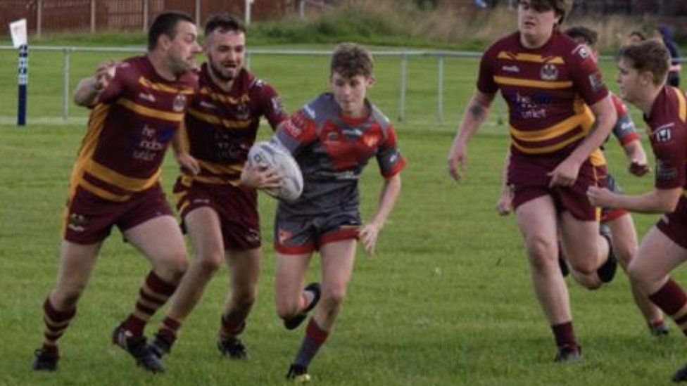 A rugby player runs between several players carrying the ball