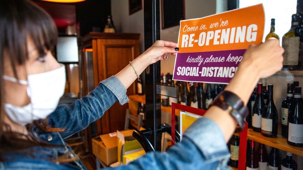 Bar owner in mask putting up reopening sign