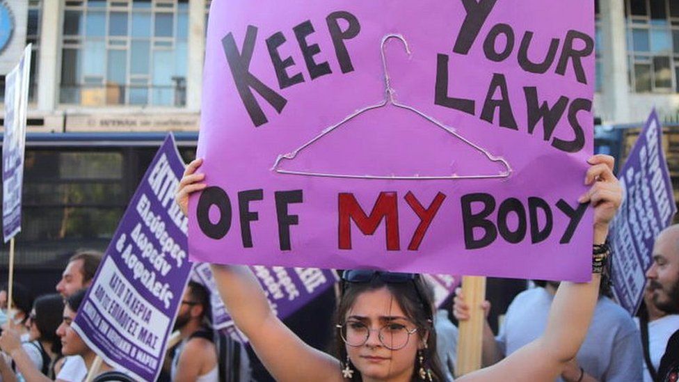 young woman holding sign reading 'keep your laws off my body'