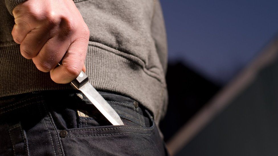 Stock image of model pulling a knife from pocket of their jeans