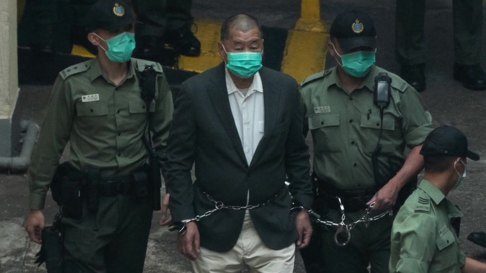 Jimmy Lai is flanked by police guards and has chains around his waist and wrists as he's taken to court after being charged under the national security law, in Hong Kong, December 12th 2020