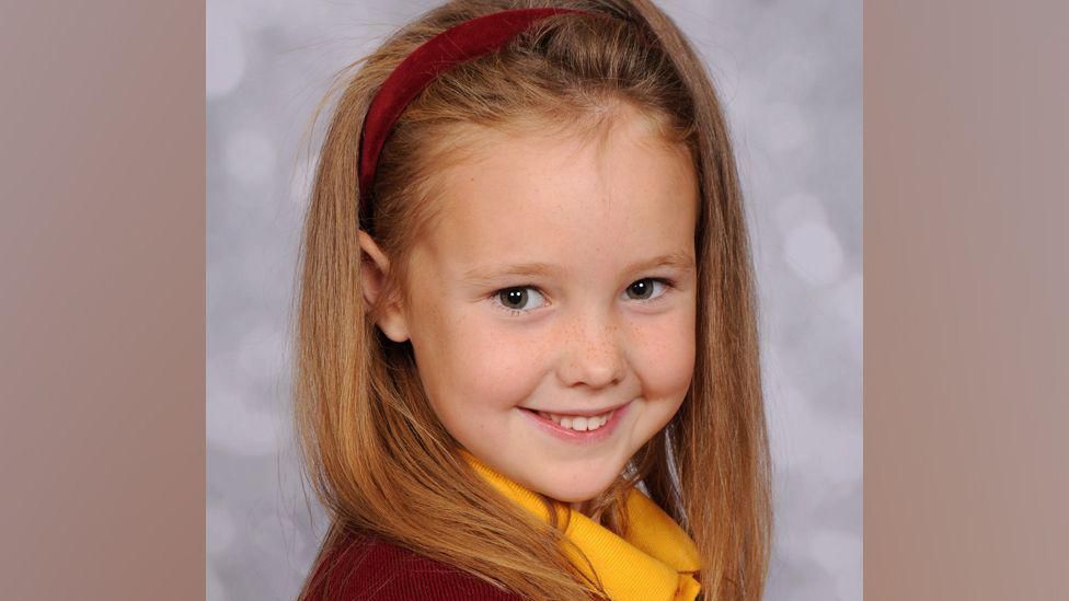  Elsie Dot Stancombe smiles for a photography while wearing a yellow polo shirt and red headband