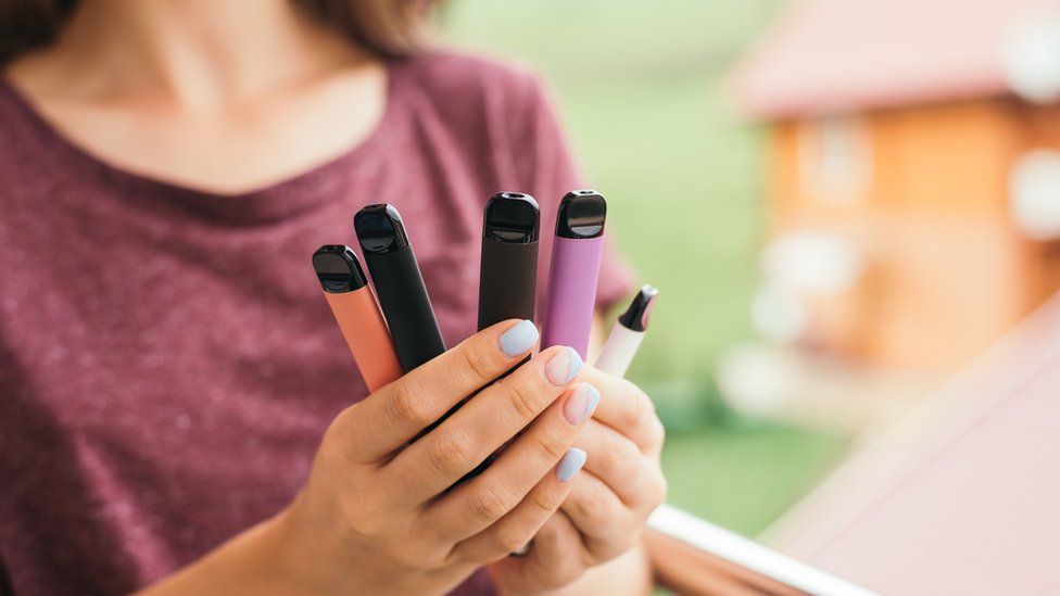 Young woman holding several coloured disposable vapes in her hand