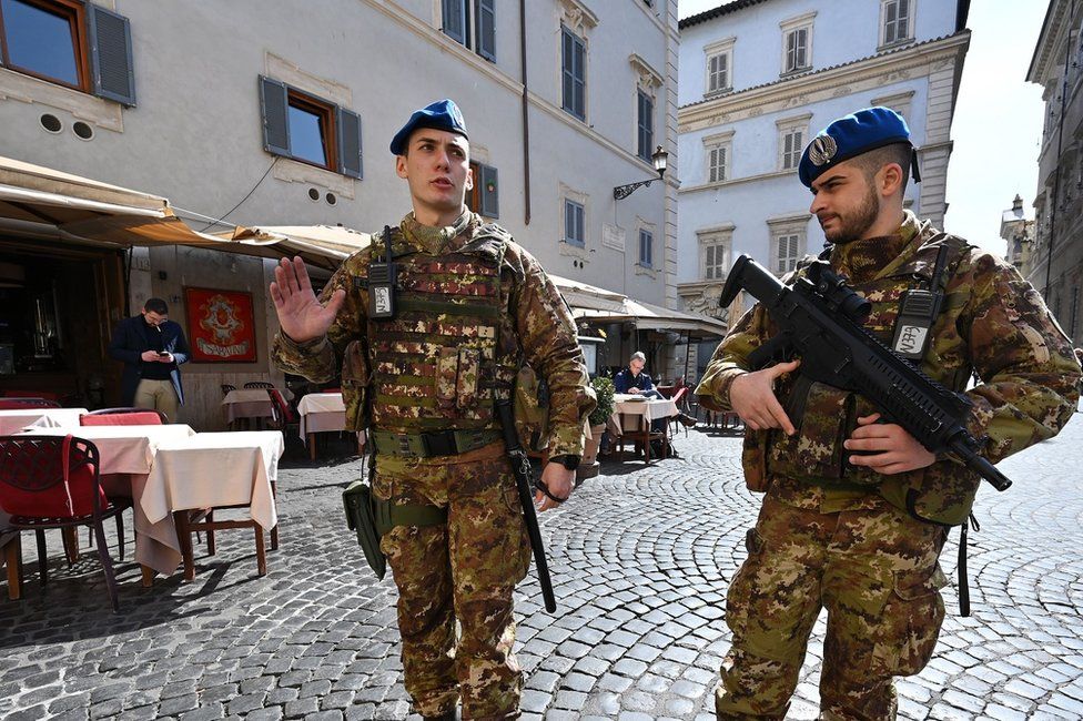 Soldiers with guns walk through a street in Rome