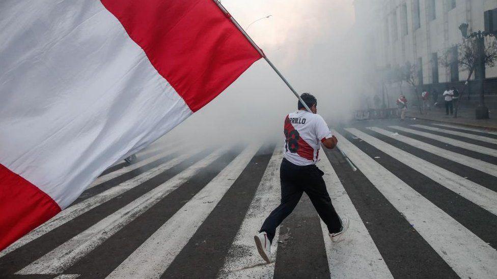 A protester with a Peruvian flag wanders through a cloud of tear gas