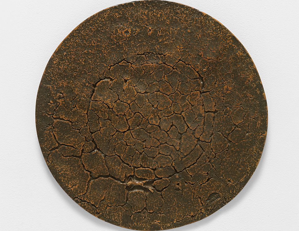 A circular bronze sculpture which gives the impression of cracked earth