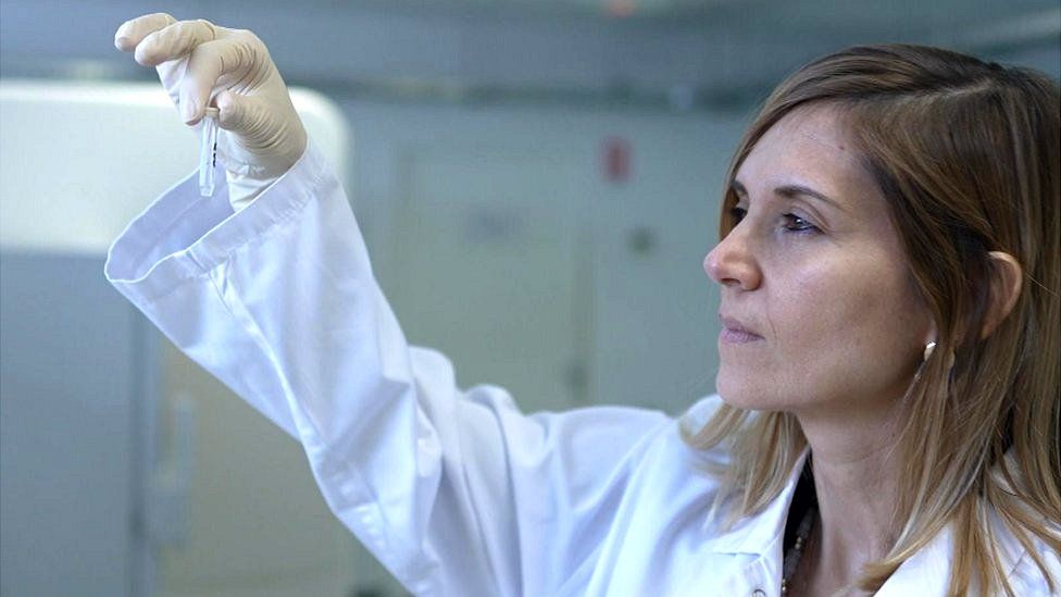 Dr Mathilde Touvier is wearing a white lab coat, with her right hand she is holding up a small test tube and looking at it