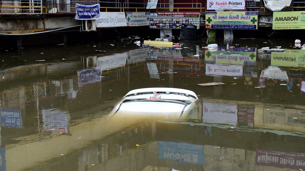 Люди смотрят на затопленный автомобиль в затопленном коммерческом комплексе после проливных дождей в Ахмадабаде, 11 июля 2022 г.