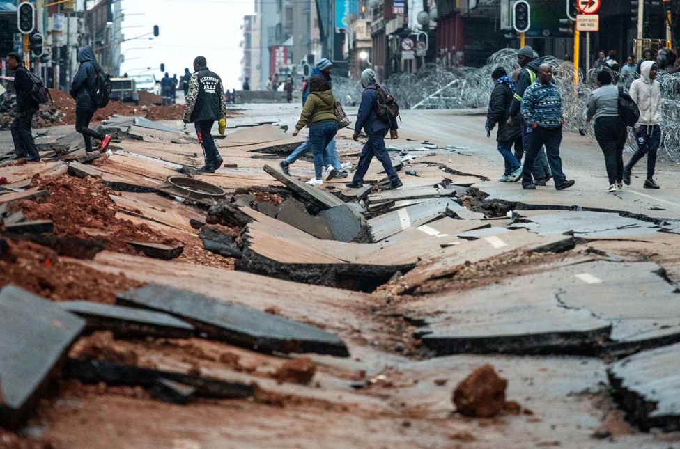 People cross a damaged street following an underground gas explosion in downtown Johannesburg, South Africa, 21 July 2023.