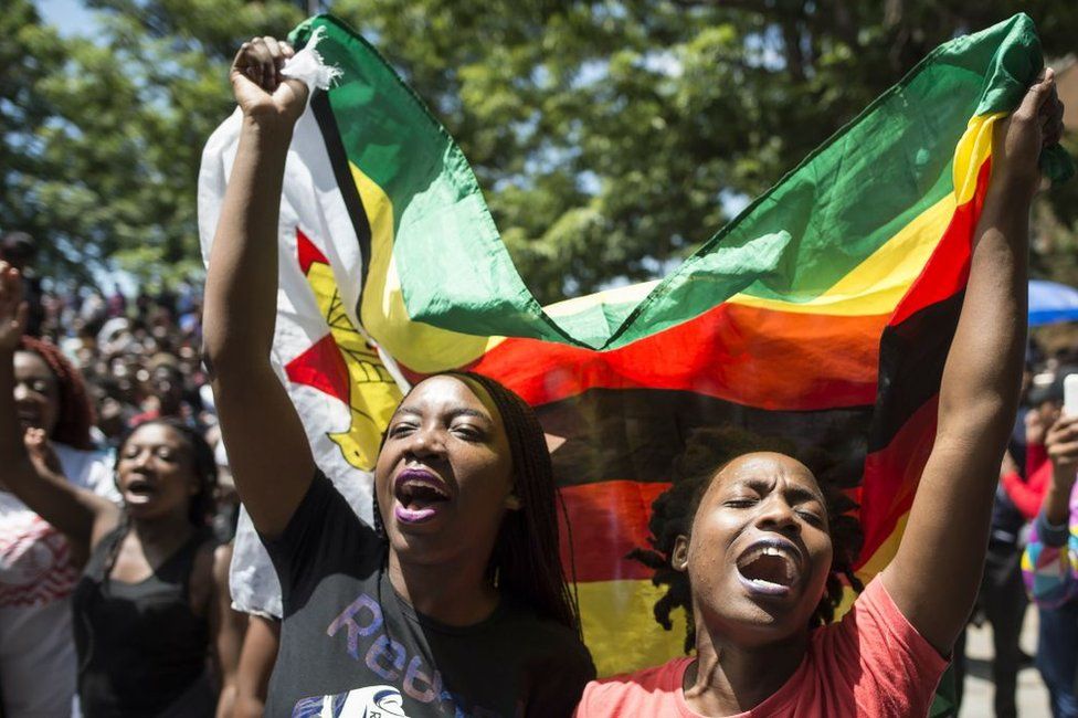 Женщины с флагом Зимбабве принимают участие в демонстрации студентов Зимбабвийского университета 20 ноября 2017 года в Хараре, поскольку на президента Зимбабве Роберта Мугабе нарастает давление с целью заставить его уйти в отставку, а также после критики его жены Грейс.