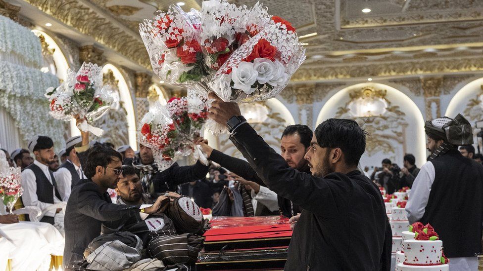 Afghan volunteers distribute flower bouquets to the grooms during a mass wedding ceremony at a wedding hall in Kabul