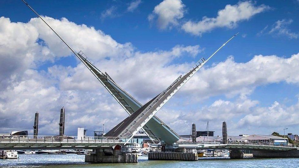 The two triangular leaves of the Twin Sails bridge in a cross position with buildings of Poole's skyline behind