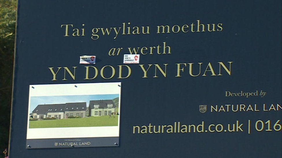 Welsh language campaign stickers on a sign advertising property for sale at Plas Pistyll, Gwynedd