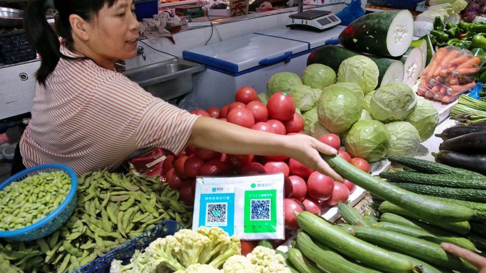 A woman sells fruit and vegetables in a Chinese market stall with a QR code on display