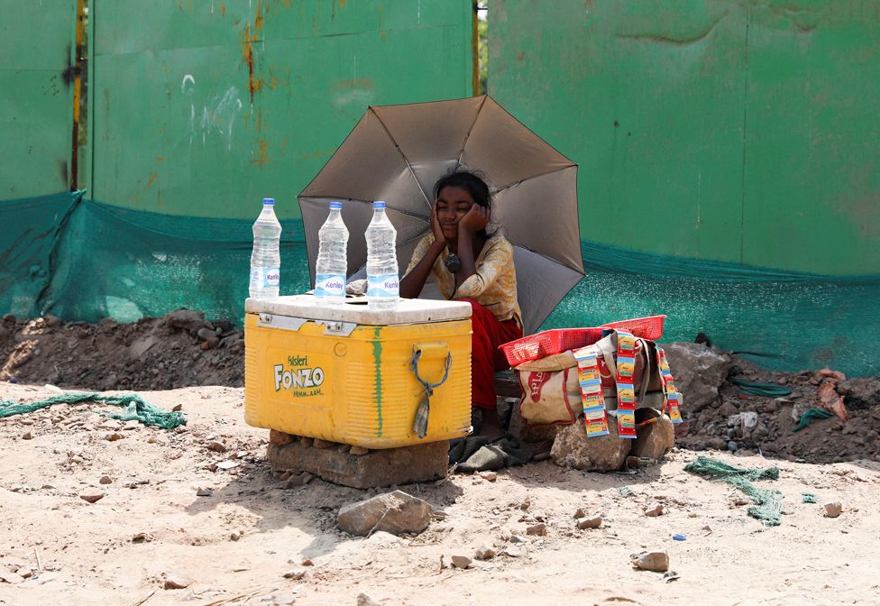 A girl selling water uses an umbrella to protect herself from the sun in Delhi, India, on 27 April 2022