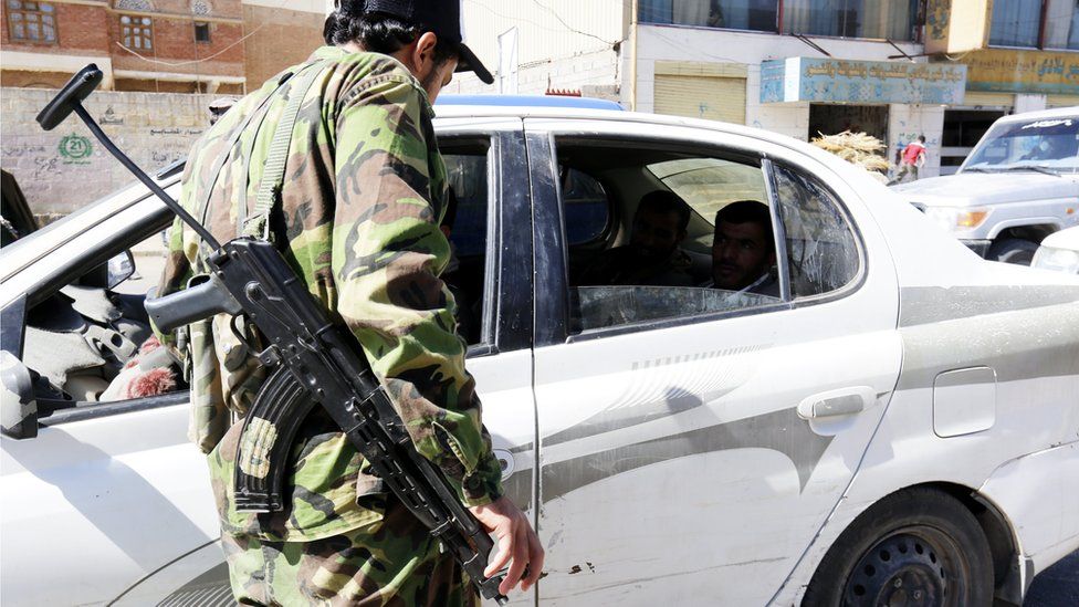 A Houthi rebel with a big gun standing outside the window of a car