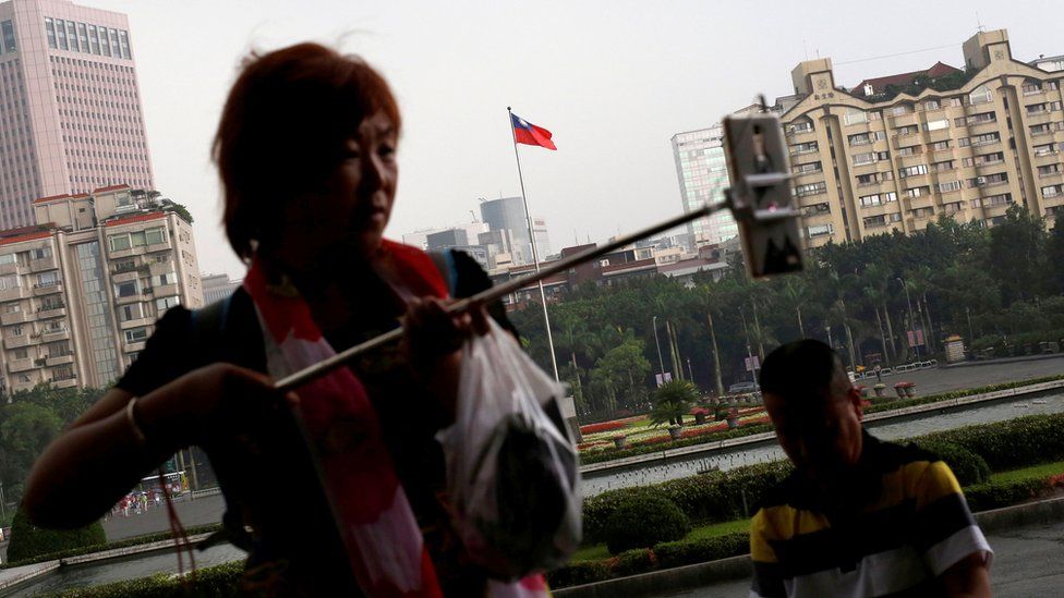 A tourist from China takes a selfie in front of a Taiwanese flag, in Taipei