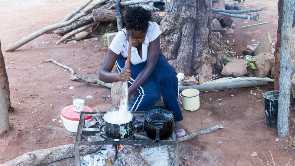 A woman cooks a typical dish, called Sadza (or Ugali, nshima, pap, phutu) on a saucepan and a fire pit