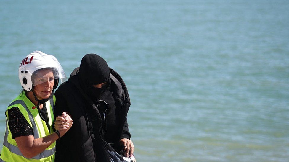 A member of the Royal National Lifeboat Institution helps a migrant on the beach at Dungeness on the southeast coast of England, on August 16, 2023