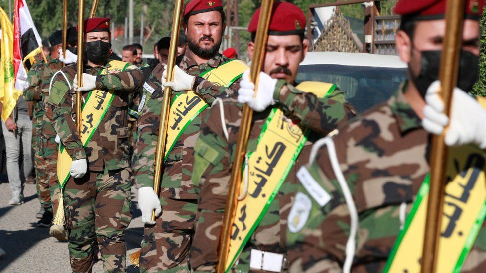 Fighters lift flags of Iraq and paramilitary groups, including Kataib Hezbollah, during a funeral in Baghdad for five militants killed in a US strike in northern Iraq, on 4 December 2023